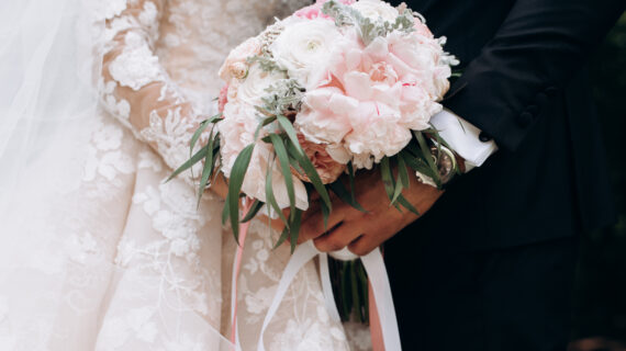 Frontview of groom and brides hands together are holding wedding pink bouquet