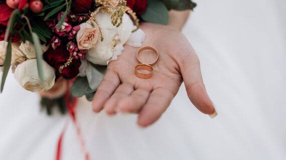 Wedding rings on the woman's hand, wedding bouquet of red and white flowers, wedding details
